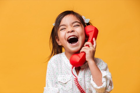 A young girl laughing into a red telephone handset